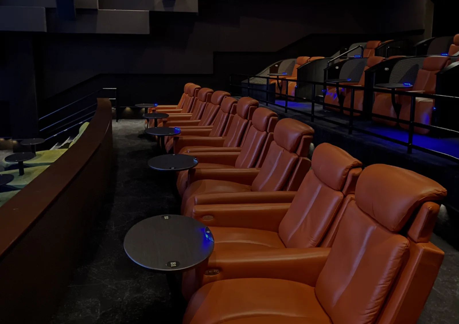 Leather recliners line a luxury movie theater with in-seat dining tables.