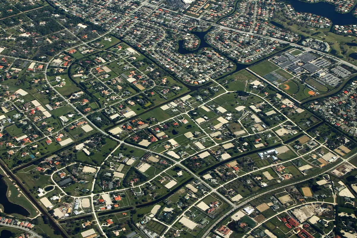 Ranch lots, barns and riding rings in Wellington's horse country, with suburban neighborhoods beyond, seen from the air.