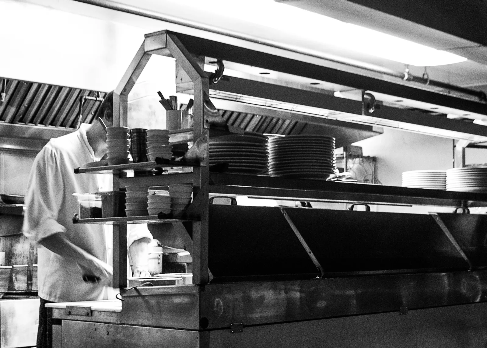 A line cook at work behind the pass in a restaurant kitchen.